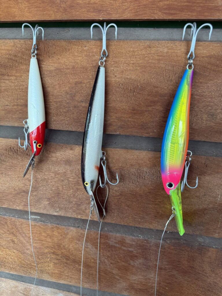 Three fishing lures with treble hooks hang on a wooden surface.