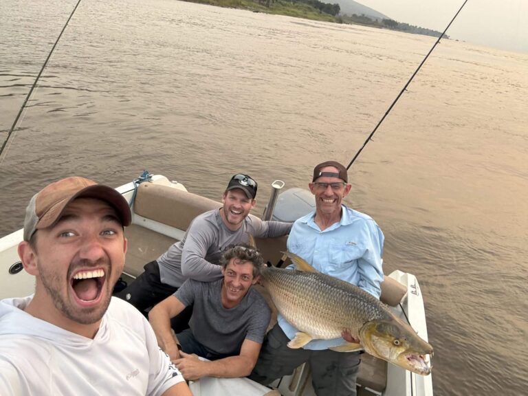 Four men proudly display a large fish they caught while on a boat.