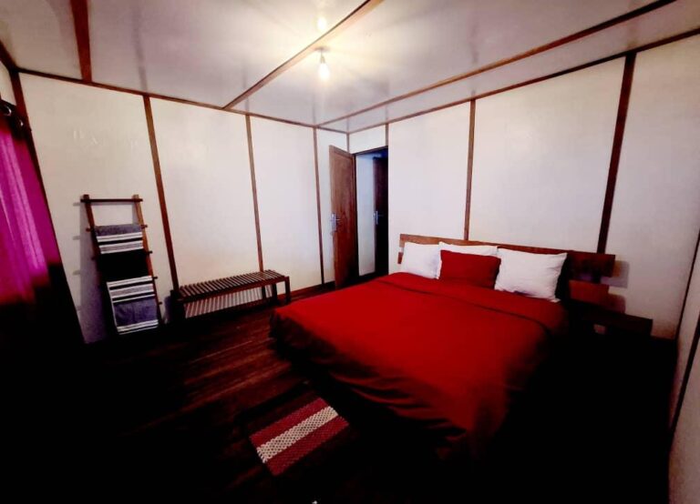 A bright red comforter covers a bed in a room with wooden accents and white walls.